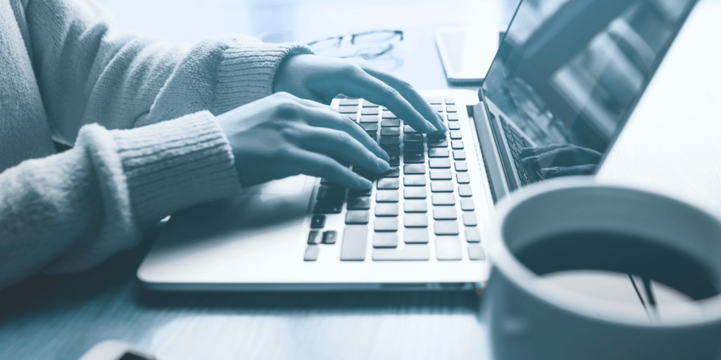 An image of a person's hands typing on a laptop shot from the side. The person is transcribing a podcast episode to optimize the podcast for search engines.